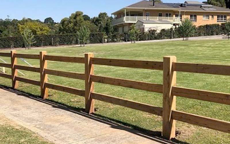 A post and rail wooden fence adorned with trees growing along its length