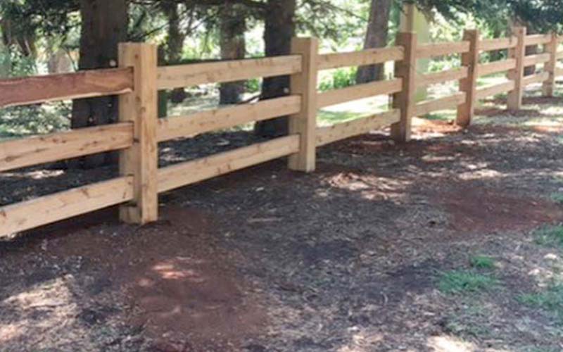 A post and rail fence with wooden posts and a wooden gate, providing a rustic and charming boundary