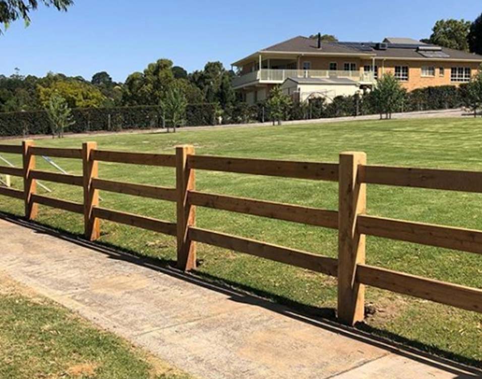 A post and rail fence with wooden posts and a wooden gate, providing a rustic and charming boundary